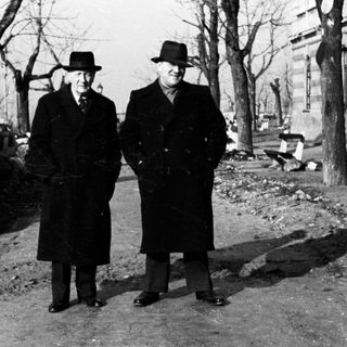 Two men in coats and hats stand outdoors.