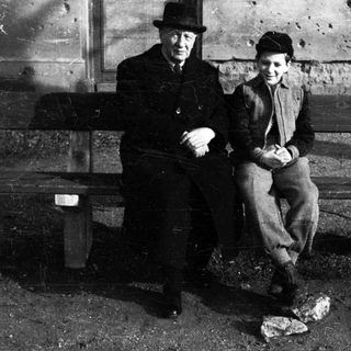Two figures sit on a bench in a textured environment.