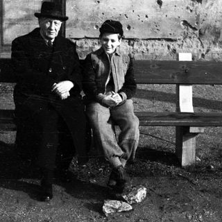 Two figures sit on a bench in a textured environment.