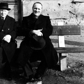 Two men seated on a bench with visible damage nearby.