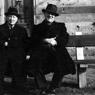 Two men in hats sit on a park bench.
