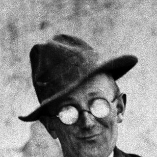 Man in a hat and vest poses outdoors.