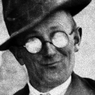 Man in a hat and vest poses outdoors.