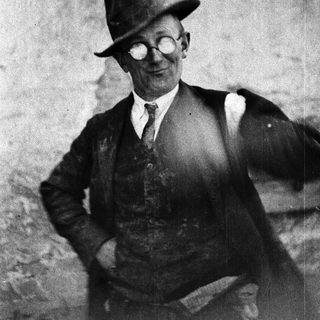 Man in a hat and vest poses outdoors.