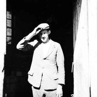 Man in hat salutes, standing in a doorway.