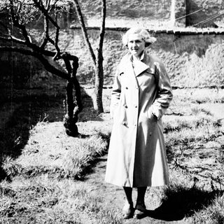 Woman stands outdoors near a wall and bare tree.