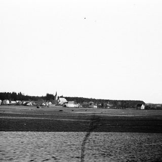 Black and white image shows a village and open fields.