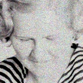 Here's a brief summary of the image: Woman seated, striped shirt, looking downward in a room.