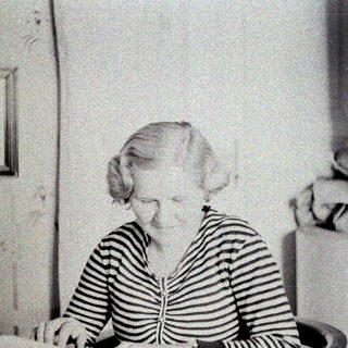 Here's a brief summary of the image: Woman seated, striped shirt, looking downward in a room.
