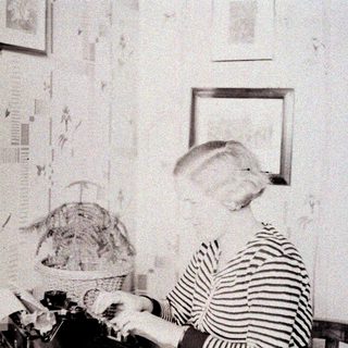 Here's a brief summary of the image: Woman seated at a desk, working on a typewriter.