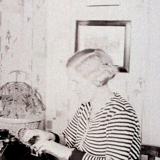 Here's a brief summary of the image: Woman seated at a desk, working on a typewriter.