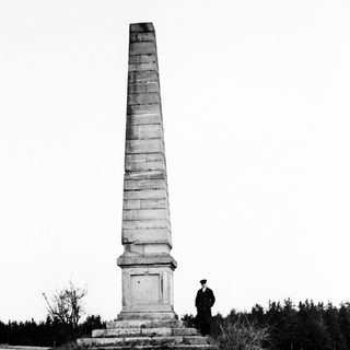 Monument stands in a field, a person nearby.