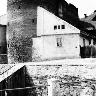Ruined tower adjacent to a house, monochrome photograph.