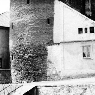 Ruined tower adjacent to a house, monochrome photograph.