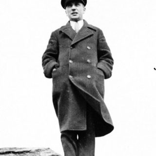Man in coat stands on rocky ledge, overlooking a view.