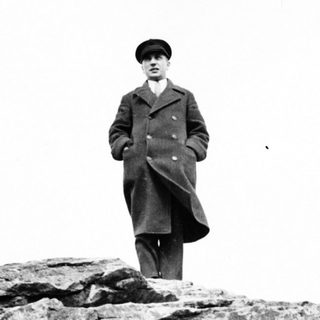 Man in coat stands on rocky ledge, overlooking a view.
