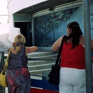 People view a mural outdoors in a public space.