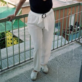 Woman stands on a balcony, wearing casual clothing.