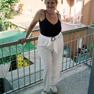 Woman stands on a balcony, wearing casual clothing.