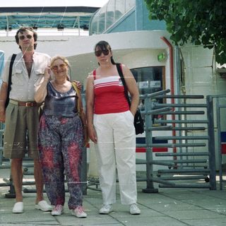 Three people stand near a building entrance, outdoors.
