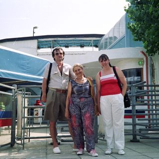 Here's a brief summary of the image: Three people posing outdoors near a building with signage.