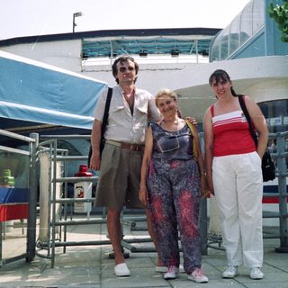 Here's a brief summary of the image: Three people posing outdoors near a building with signage.