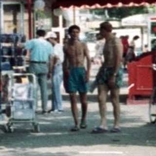 People walk past a cafe on a sunny street.