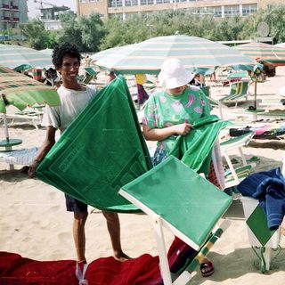 Beach attendant sets up chairs for guests on a sunny day.
