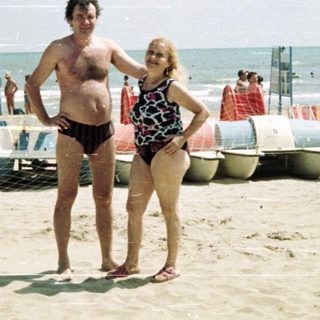 Couple stands on a crowded beach near the ocean.