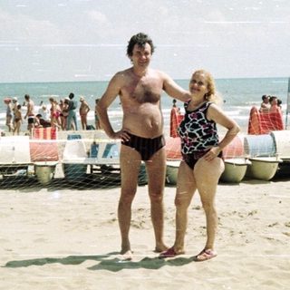 Couple stands on a crowded beach near the ocean.
