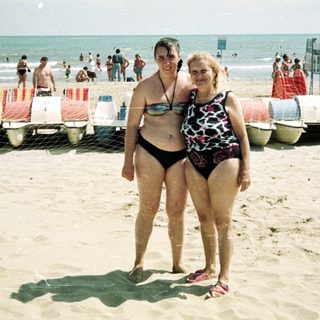 Two women stand on a crowded beach near the ocean.