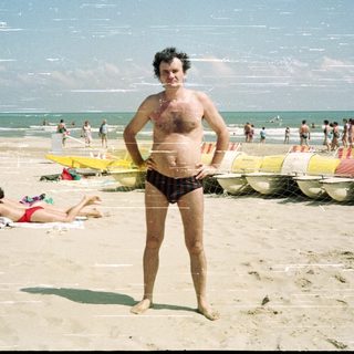 Man stands on a crowded beach with the ocean behind.