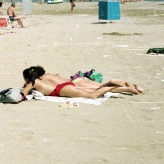 Woman walks on crowded beach with ocean in background.