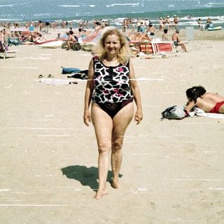 Woman walks on crowded beach with ocean in background.