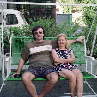 Couple sits on a swing in a garden setting.