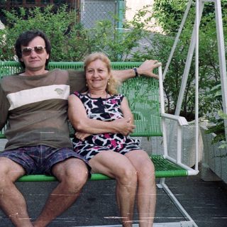 Couple sits on a swing in a garden setting.