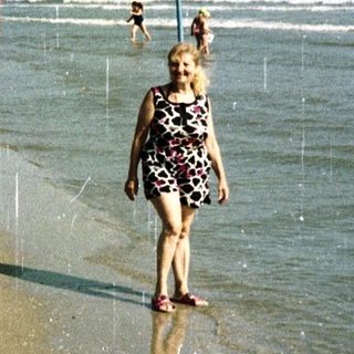 Woman walking on a crowded beach with the ocean behind.