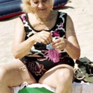 Crowded beach scene with a woman sitting on a chair.