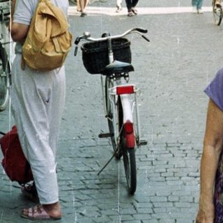 Woman stands on a cobblestone street in a town.
