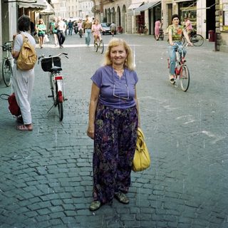 Woman stands on a cobblestone street in a town.