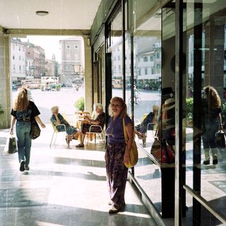Woman stands in a covered walkway, overlooking a town square.