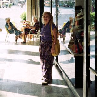 Woman stands in a covered walkway, overlooking a town square.