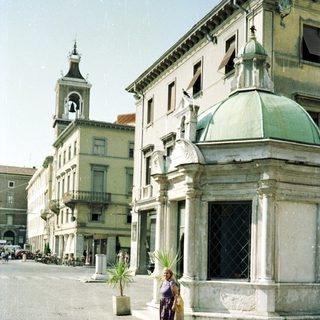 Woman stands in a square with historic buildings.