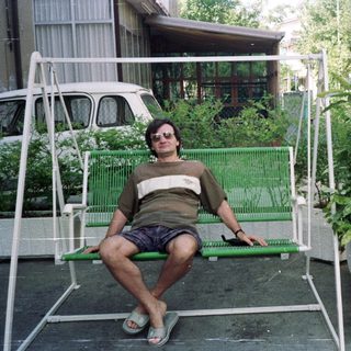 Man sits on a swing outside a house.