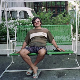 Man sits on a swing outside a house.