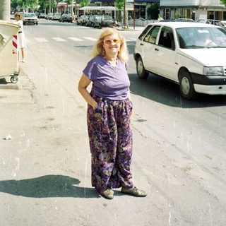 Woman in patterned pants stands on a city street.