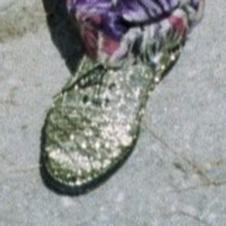 Woman stands near a wall, wearing vibrant patterned pants.