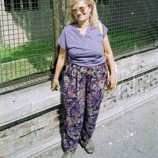 Woman stands near a wall, wearing vibrant patterned pants.
