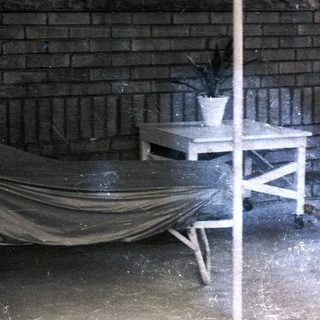 Woman sits on porch with furniture and plants.