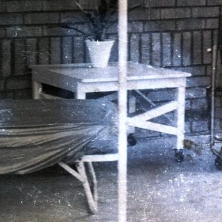 Woman sits on porch with furniture and plants.
